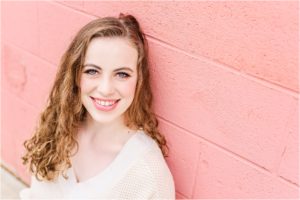 senior girl smiling against a pink wall